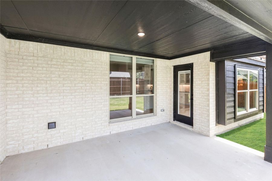 Covered patio with concrete floor, white brick walls, dark ceiling, and glass back door leading to backyard