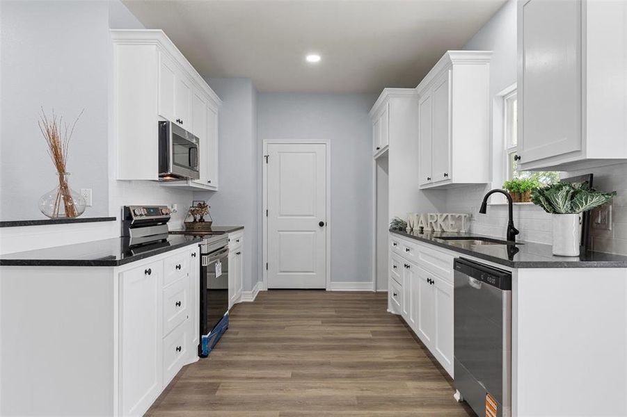 Kitchen with stainless steel appliances, dark stone counters, white cabinets, dark wood-type flooring, and recessed lighting