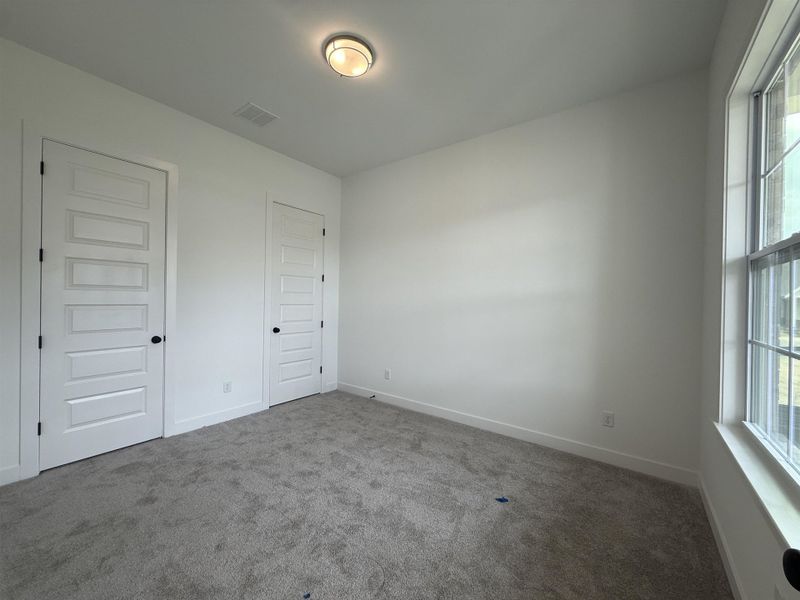 Carpeted room with white walls and trim, featuring a flush-mount ceiling light fixture, two panel doors, and a window
