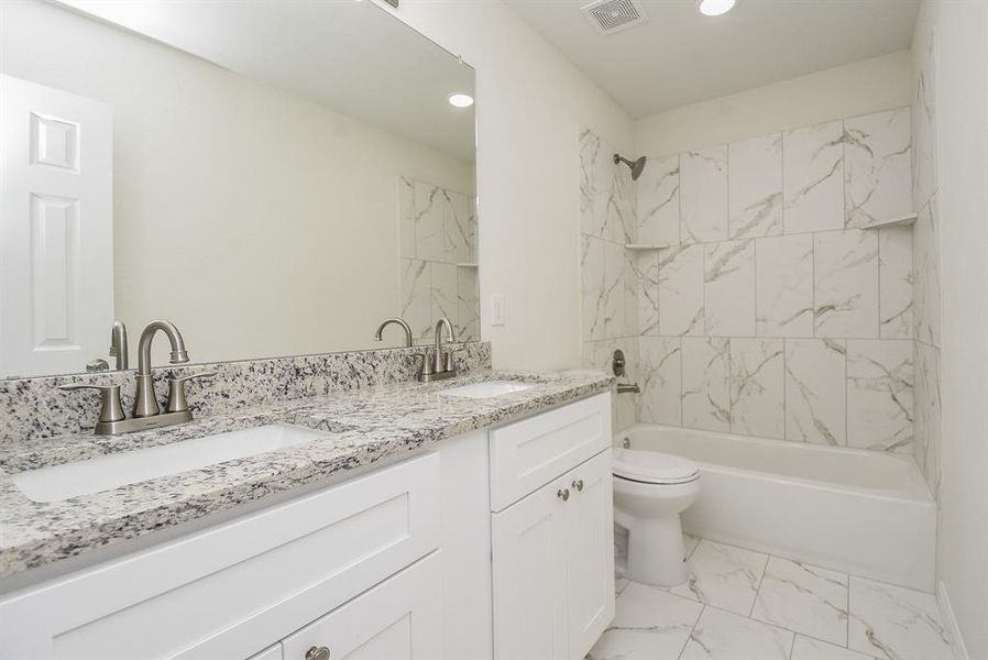 Modern bathroom with white cabinets, granite countertops, dual sinks, large mirror, and a shower-tub combo with marble-like tile walls.