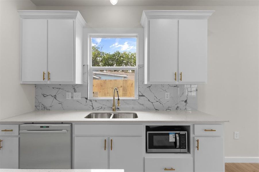 Kitchen featuring white cabinetry with gold-finish hardware, a white countertop, and a marble-patterned backsplash