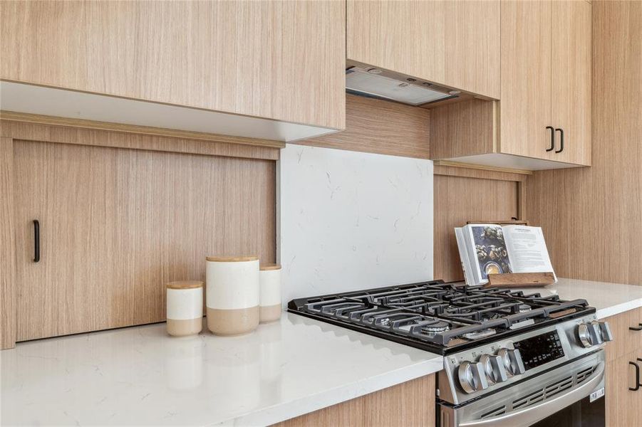 Sleek and modern kitchen design featuring warm cabinetry, a stylish gas range, and elegant quartz countertops. Thoughtful details like hidden storage and a minimalist backsplash create a seamless, functional space perfect for cooking and entertaining.