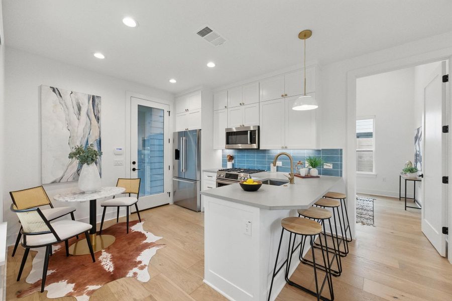 Kitchen with tasteful backsplash, decorative light fixtures, white cabinetry, light wood finished floors, and stainless steel appliances Kitchen with tasteful backsplash, decorative light fixtures, white cabinetry, light wood finished floors, and stainless steel appliances