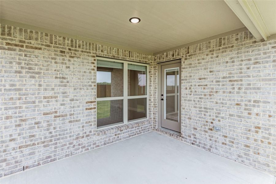 Covered back patio with light brick walls, glass door, and recessed ceiling light