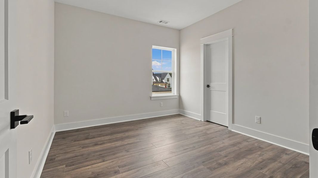 Spacious bedroom with hardwood flooring with one window and closet space.