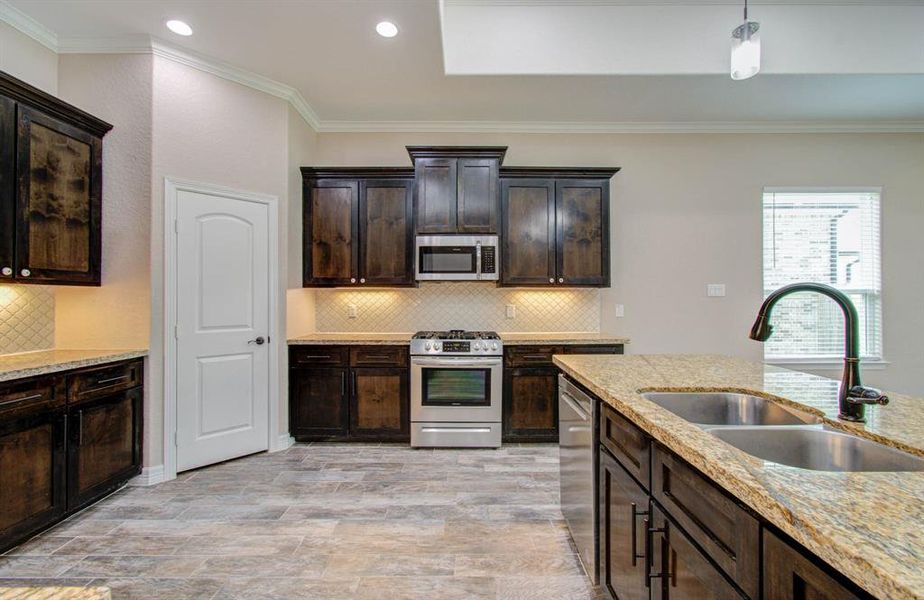 This is a modern kitchen featuring dark wood cabinetry, granite countertops, stainless steel appliances, and a tiled floor. A window provides natural light.