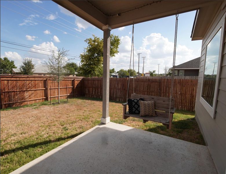 A covered concrete patio overlooks the wood-fenced backyard under clear blue skies. A covered concrete patio overlooks the wood-fenced backyard under clear blue skies.