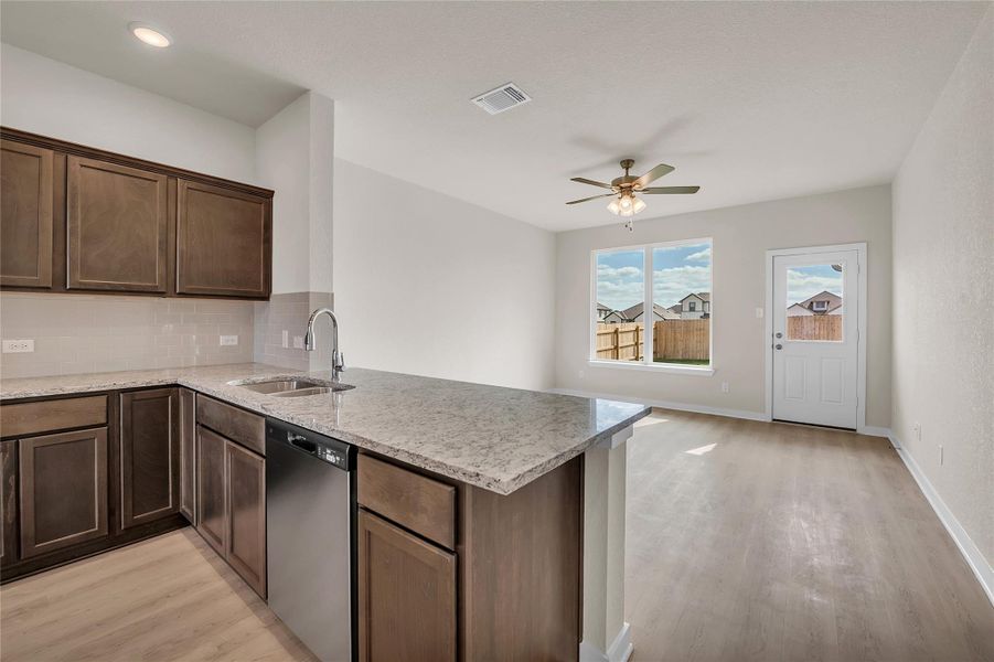Kitchen with light stone counters, tasteful backsplash, stainless steel dishwasher, ceiling fan, and light wood finished floors