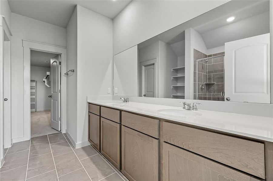 Full bathroom featuring a spacious closet, double vanity, a shower stall, and light tile patterned floors Full bathroom featuring a spacious closet, double vanity, a shower stall, and light tile patterned floors