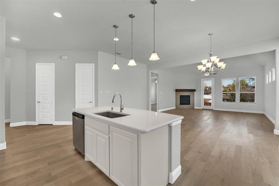 Kitchen featuring a fireplace, a center island with sink, open floor plan, suspended lighting, and white cabinetry