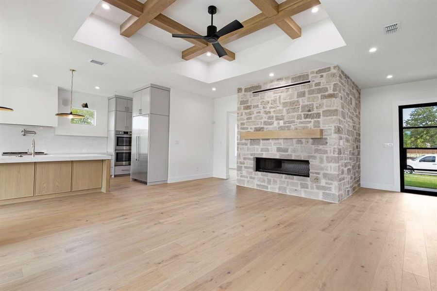 Unfurnished living room featuring sink, beam ceiling, a fireplace, light hardwood / wood-style flooring, and ceiling fan