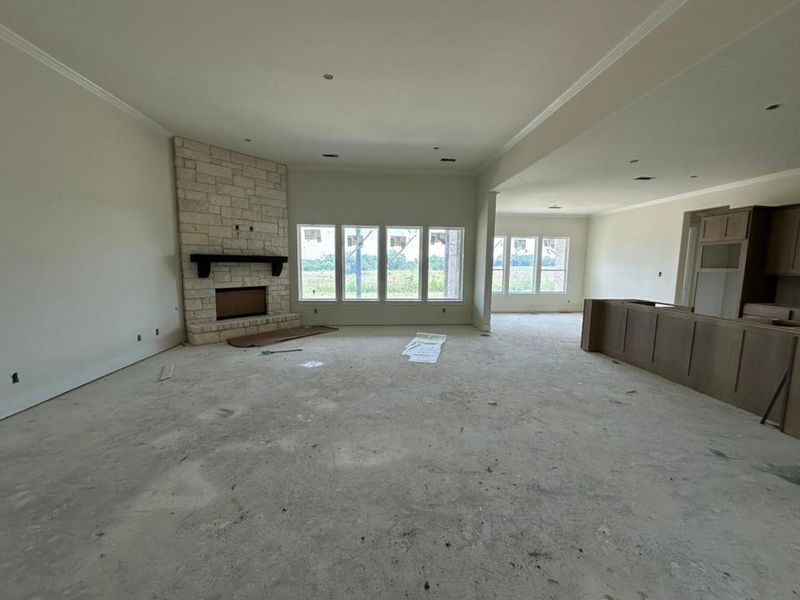 Spacious interior featuring a stone fireplace with a dark wood mantel, multiple windows, high ceilings with crown molding, and partial cabinetry