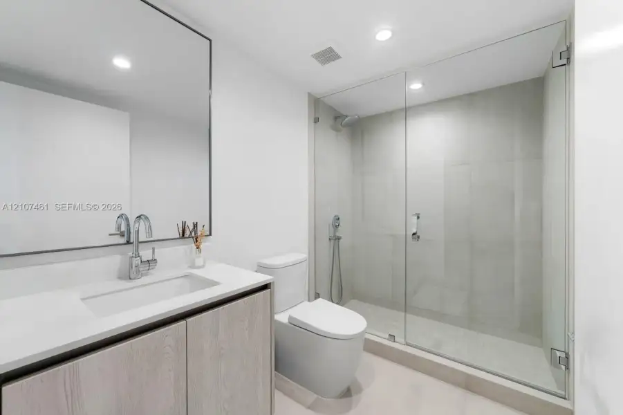 Bathroom featuring a wood-finish vanity with a stone countertop, an integrated rectangular sink, a wall-to-wall mirror, and a walk-in shower with a glass enclosure and tiled walls Bathroom featuring a wood-finish vanity with a stone countertop, an integrated rectangular sink, a wall-to-wall mirror, and a walk-in shower with a glass enclosure and tiled walls