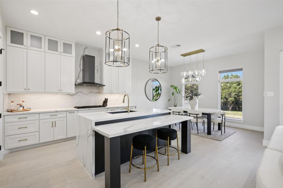 Kitchen featuring white cabinets, glass insert cabinets, backsplash, light stone countertops, and a breakfast bar area
