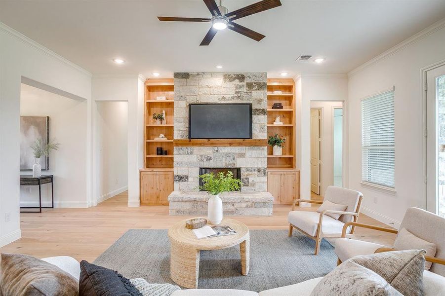 Living area with built in adjustable shelves, light engineered wood flooring, a stone fireplace with solid cedar mantle, ceiling fan, and french doors that open to a covered back patio.