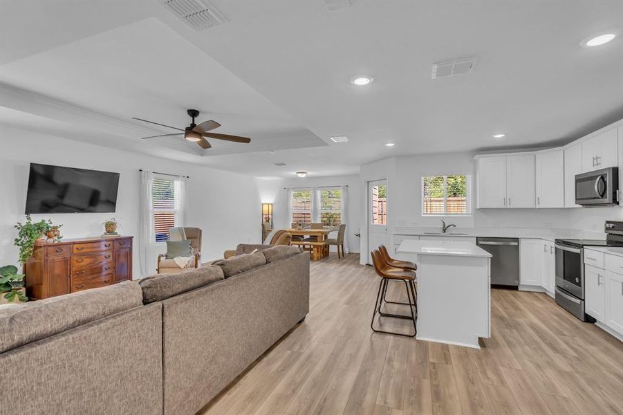 Living area with a tray ceiling, light wood-type flooring, recessed lighting, and ceiling fan