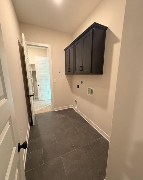 Laundry room with dark tile patterned flooring, cabinet space, washer hookup, and electric dryer hookup