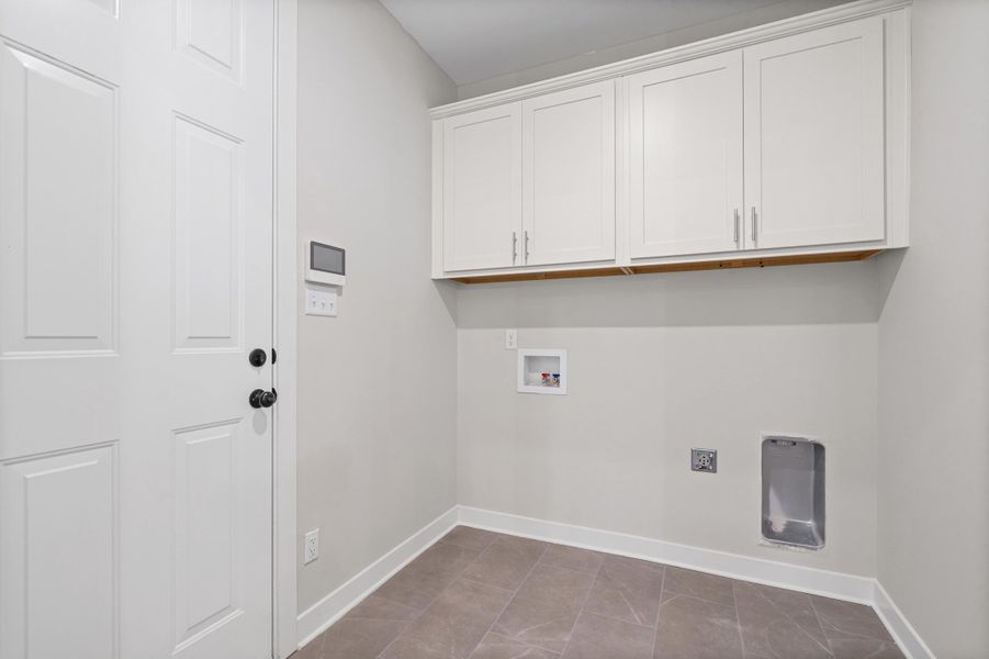 Laundry area featuring white shaker-style cabinetry, a paneled door with black hardware, and large format floor tiling Laundry area featuring white shaker-style cabinetry, a paneled door with black hardware, and large format floor tiling