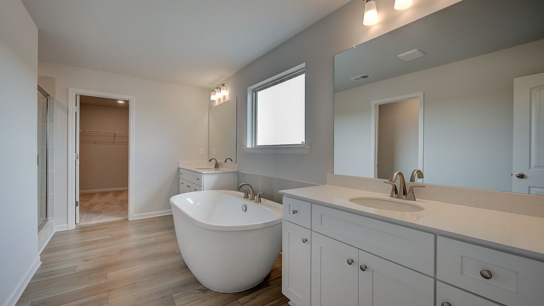 Primary bath with modern tile flooring, freestanding tub, and dual vanities in the Stonefield at Brighton.