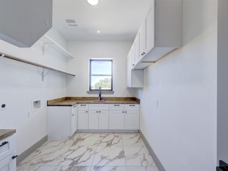 White cabinetry and marbled tile flooring define this functional utility space with a central window.