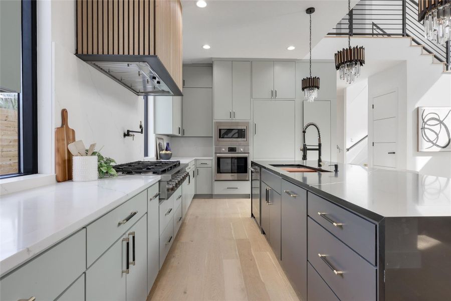 Kitchen featuring light wood-style floors, pendant lighting, stainless steel appliances, light stone counters, and a large island with sink