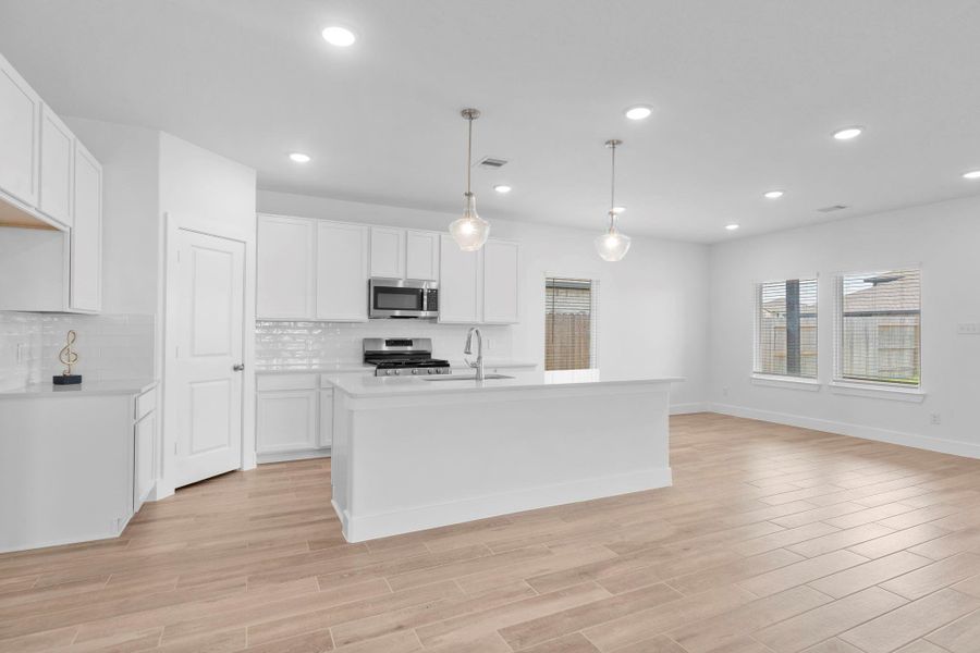 Stylish kitchen view showcasing tall white shaker cabinets, quartz countertops, and a large island with pendant lighting—make this your home, call now!