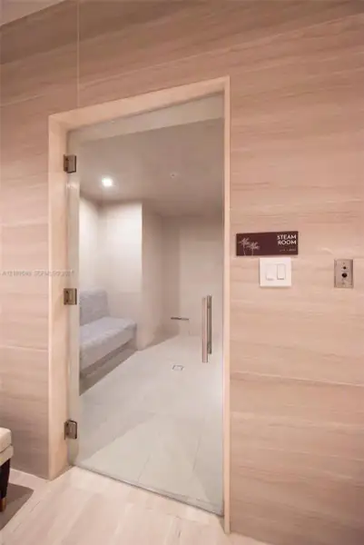 Steam room featuring large-format tile wall cladding, a frameless glass door with brushed-metal hardware, an integrated tiled bench, and recessed ceiling lighting