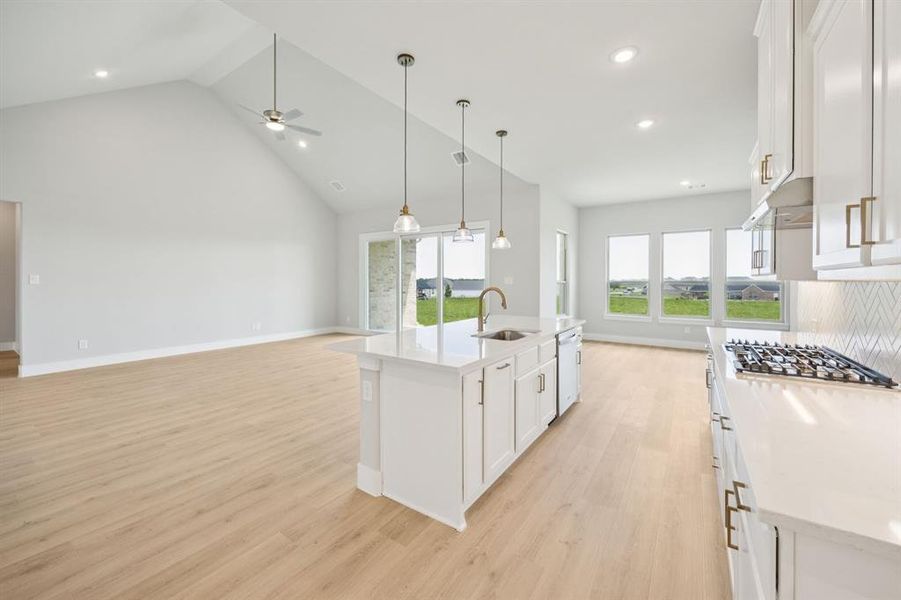 Kitchen featuring white cabinets, light stone countertops, high vaulted ceiling, an island with sink, and light wood-style floors