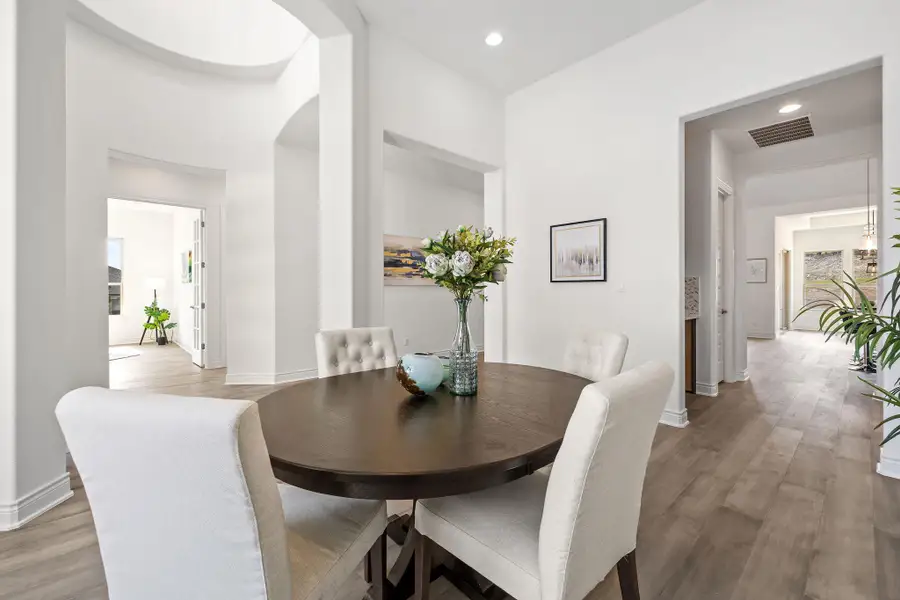 Dining area featuring light wood-style flooring, arched walkways, and recessed lighting