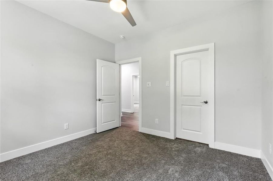 Unfurnished bedroom with dark colored carpet and a ceiling fan
