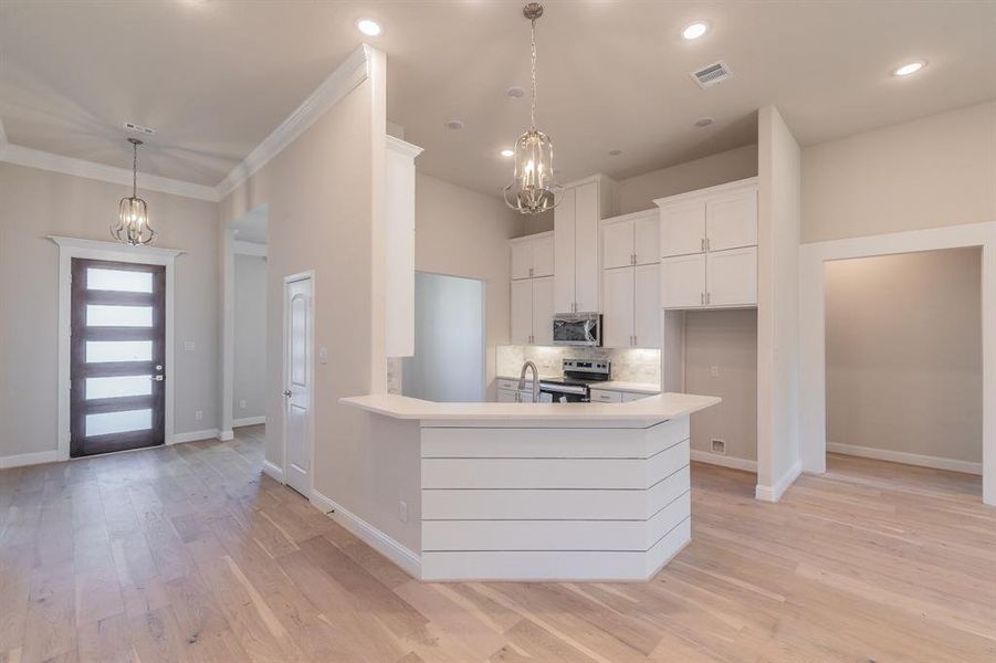 Kitchen featuring white cabinetry, tasteful backsplash, crown molding, light hardwood / wood-style floors, and appliances with stainless steel finishes