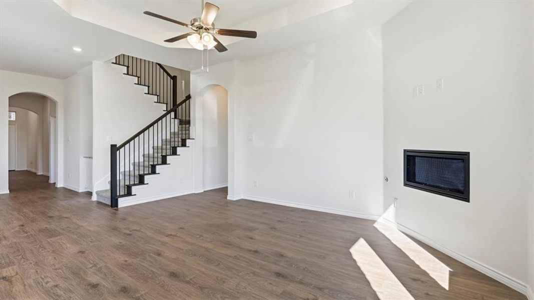 Unfurnished living room featuring stairway, dark wood-style floors, a tray ceiling, a ceiling fan, and recessed lighting Unfurnished living room featuring stairway, dark wood-style floors, a tray ceiling, a ceiling fan, and recessed lighting