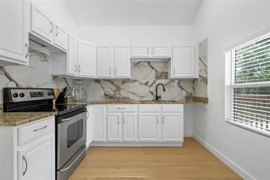 Kitchen featuring electric stove, white cabinets, stone counters, decorative backsplash, and light wood finished floors Kitchen featuring electric stove, white cabinets, stone counters, decorative backsplash, and light wood finished floors