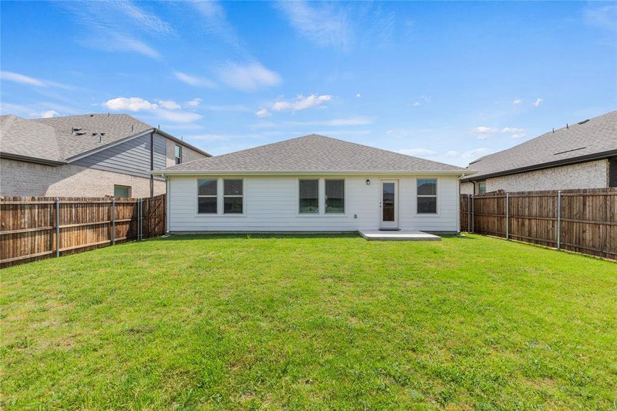 Expansive backyard featuring a manicured lawn, full perimeter wood fencing, a white siding exterior, multiple windows, and a concrete patio