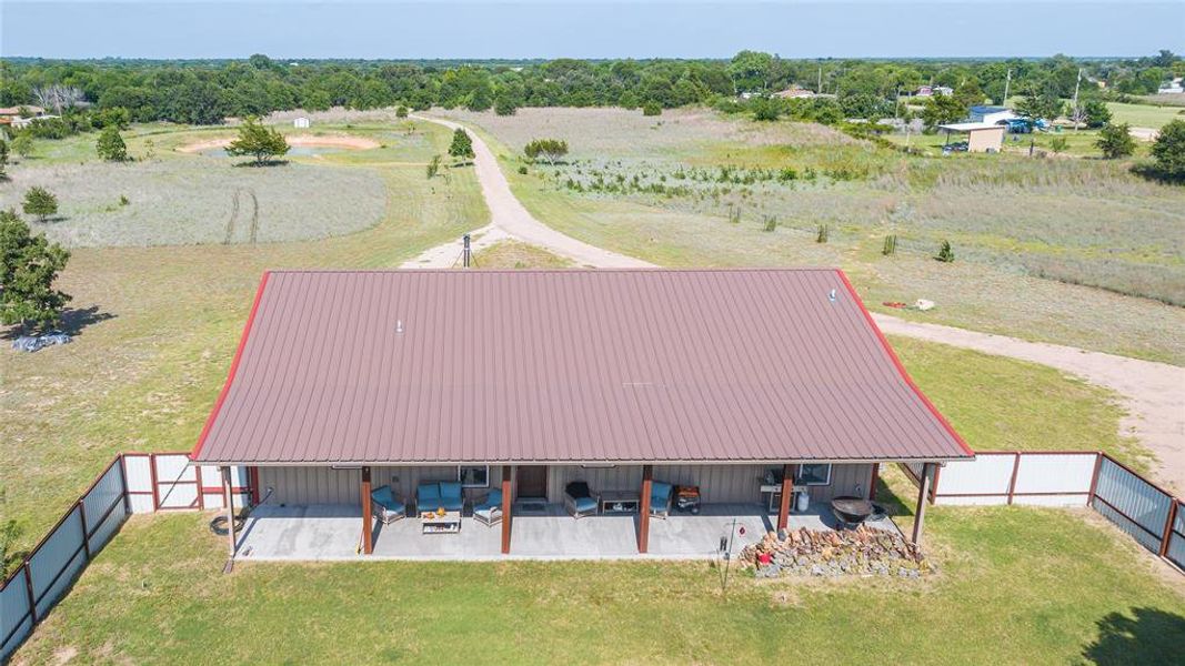 Single-story residence featuring a brown metal roof, light-colored siding, and a full-length covered porch supported by wood posts Single-story residence featuring a brown metal roof, light-colored siding, and a full-length covered porch supported by wood posts