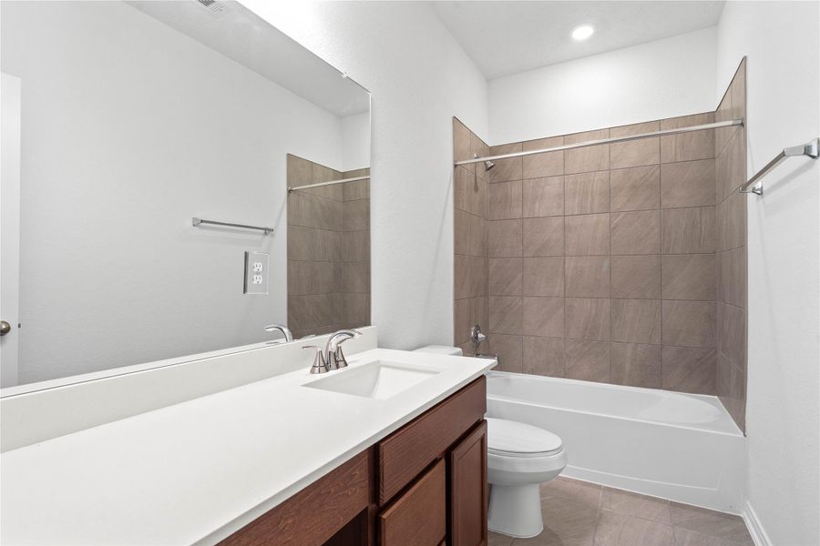 The secondary bathroom showcases tile flooring, a bath/shower combo with tile surround, a vanity with knee space and stunning light countertop, a mirror, sleek fixtures, and contemporary finishes throughout.
