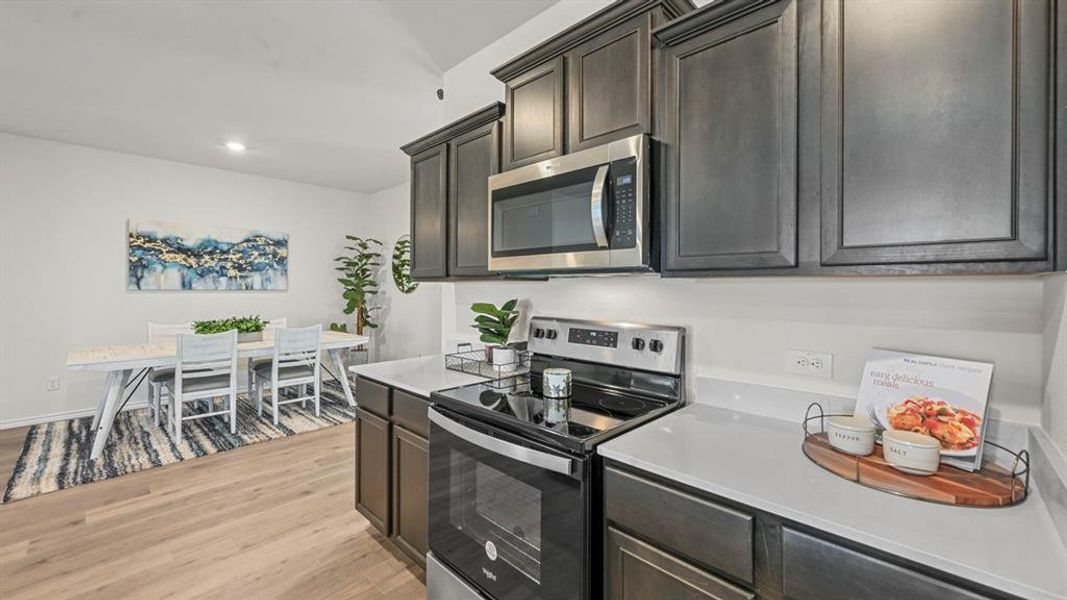 Kitchen with stainless steel appliances, light wood-type flooring, dark wood finish cabinetry, recessed lighting, and light stone countertops