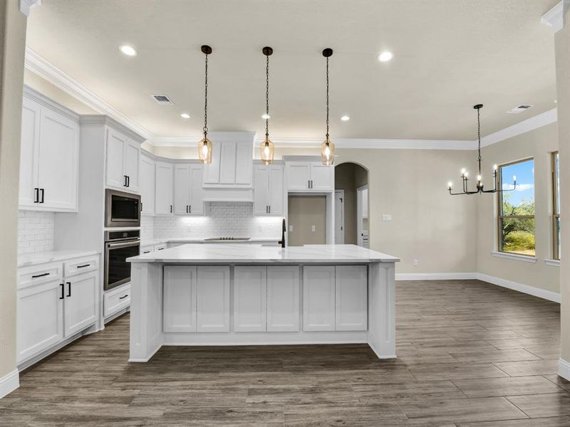 Kitchen with white cabinets, oven, built in microwave, and a kitchen island with sink