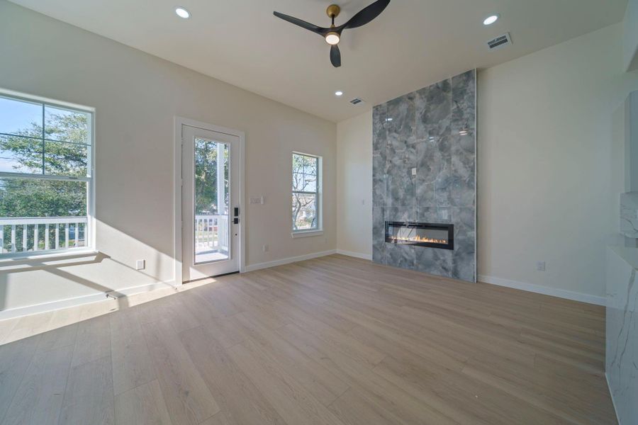 Bright and modern living room featuring a sleek fireplace with a gray porcelain surround. It has large windows, light wood flooring, and a ceiling fan, with access to an outdoor area through a glass door. Bright and modern living room featuring a sleek fireplace with a gray porcelain surround. It has large windows, light wood flooring, and a ceiling fan, with access to an outdoor area through a glass door.