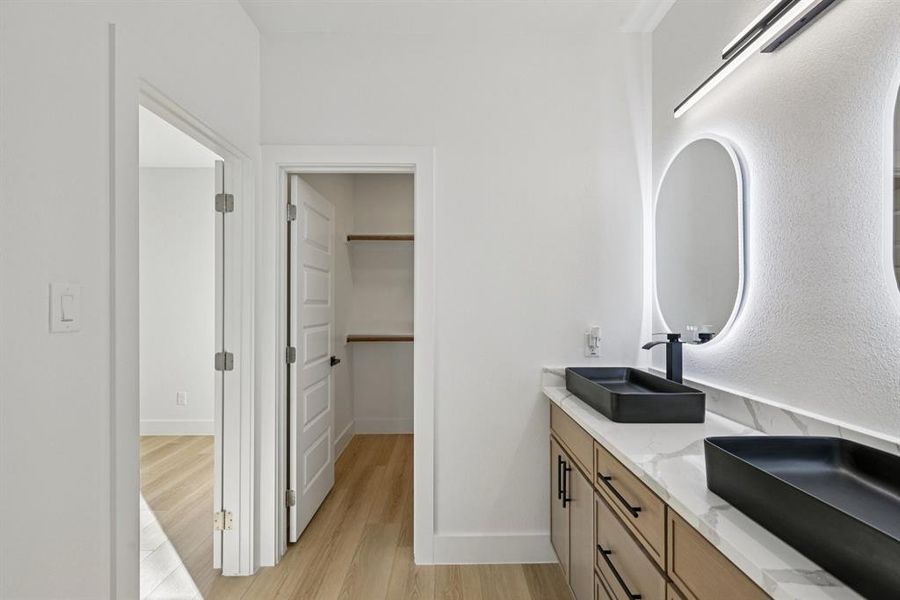 Full bathroom with double vanity, light wood-type flooring, and a walk in closet