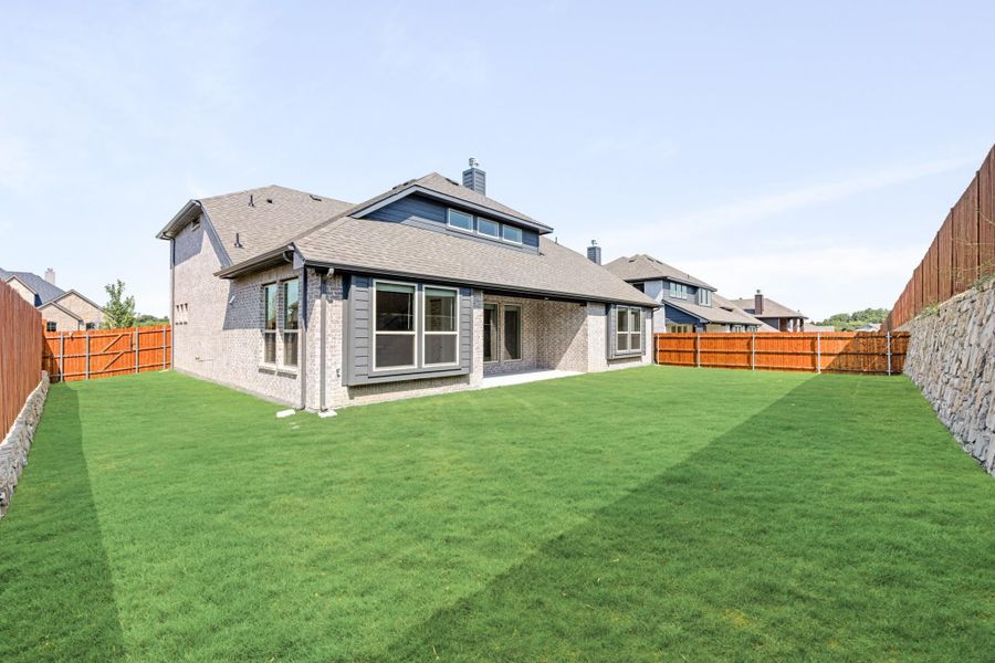 Rear view of brick home with large green backyard and wood privacy fence