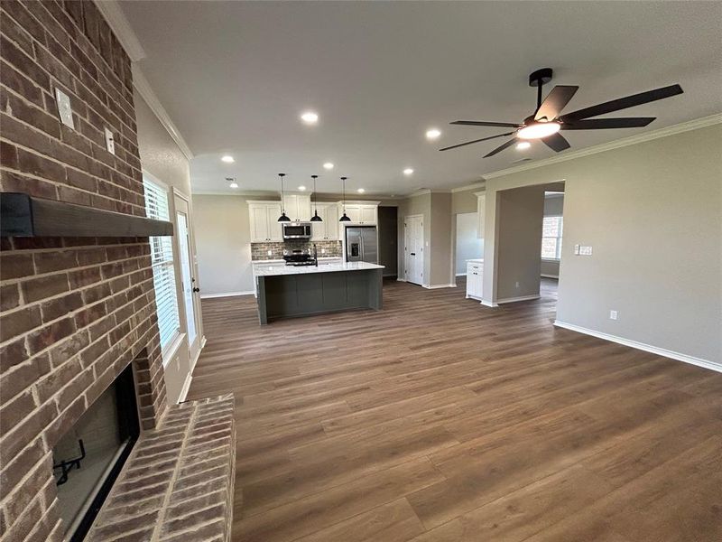 Unfurnished living room with plenty of natural light, ornamental molding, recessed lighting, dark wood-style flooring, and a brick fireplace