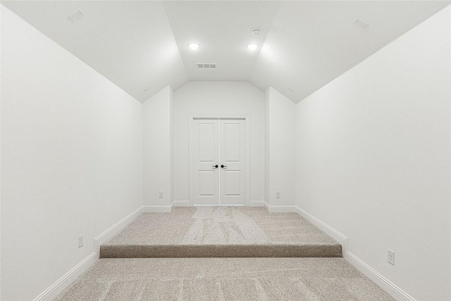 Empty room with vaulted ceiling, carpet flooring, recessed lighting, and double doors at the end Empty room with vaulted ceiling, carpet flooring, recessed lighting, and double doors at the end