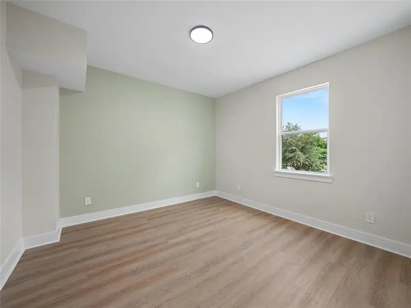 Room featuring wood-finish flooring, a single window with white trim, and a flush-mount ceiling light Room featuring wood-finish flooring, a single window with white trim, and a flush-mount ceiling light