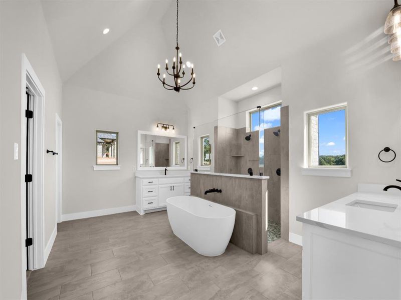 Bathroom with two vanities, a walk in shower, a freestanding bath, recessed lighting, and high vaulted ceiling
