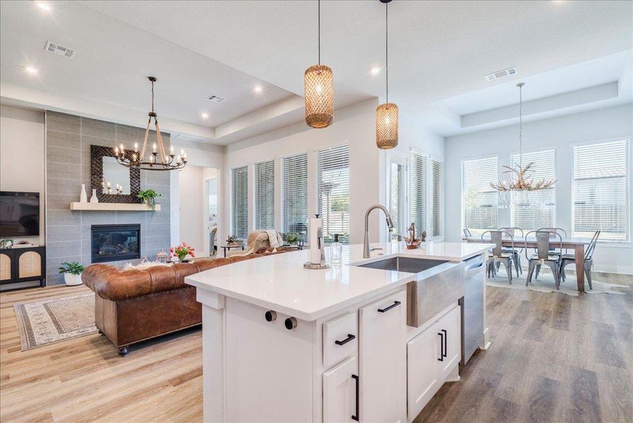 Kitchen with a chandelier, white cabinets, a raised ceiling, open floor plan, and light wood finished floors Kitchen with a chandelier, white cabinets, a raised ceiling, open floor plan, and light wood finished floors