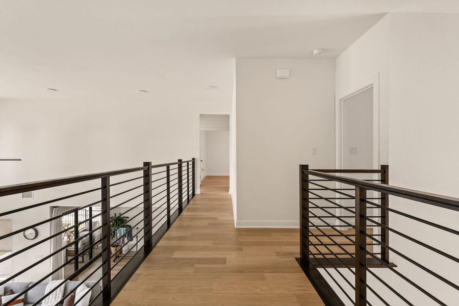 Upper-level hallway featuring wood-finish flooring, white walls, and contemporary black metal horizontal railing