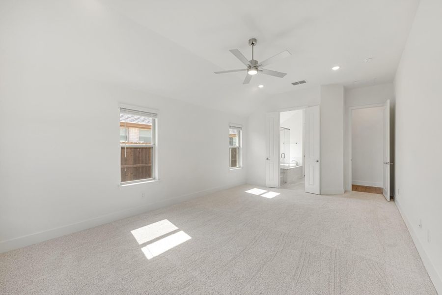 Empty bedroom with carpet flooring, ceiling fan, and ensuite bathroom doorway visible Empty bedroom with carpet flooring, ceiling fan, and ensuite bathroom doorway visible