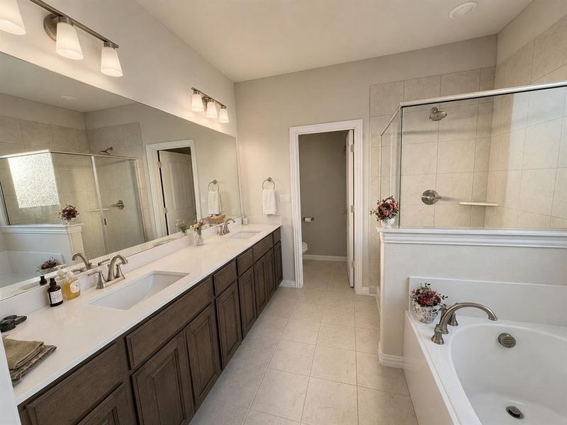 Spacious bathroom featuring a dual vanity with wood-finish cabinetry and white countertops, a walk-in shower with glass enclosure and tiled walls, a separate built-in soaking tub, and tile flooring