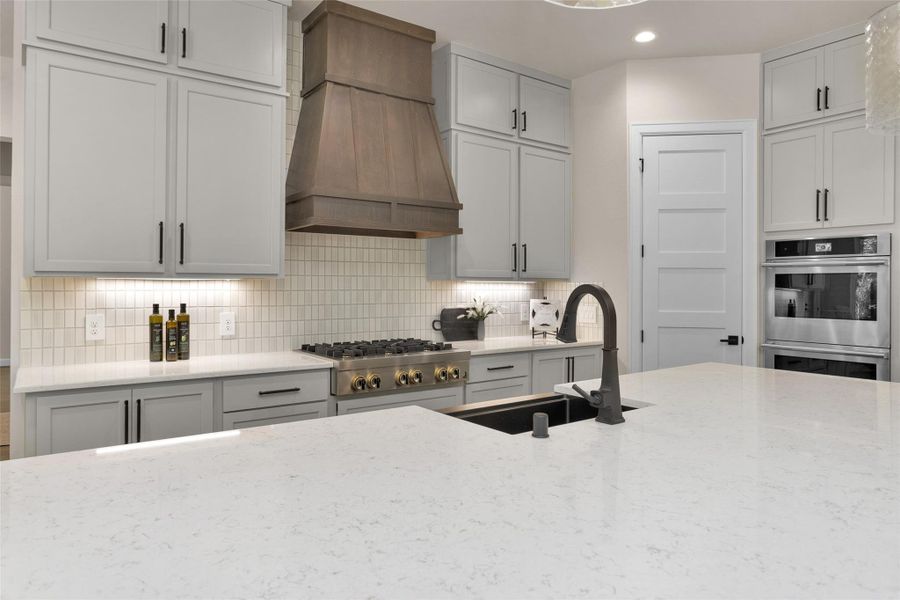 Luxury quartz countertops with soft veining pair beautifully with the textured tile backsplash while under-cabinet lighting highlights the clean lines and adds a warm, modern touch.